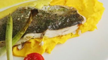 Yakın plan kızarmış balık filetosu patates püresi ve dilimlenmiş sebzeler tabakta döner.