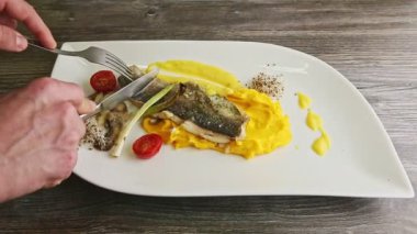 İnsan elleri bıçak ve çatal fırınlanmış deniz balığı filetosu ile servis edilir.