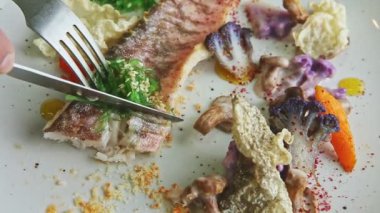 Yakından çekilen eller, küçük balık filetosunu çatal ve bıçakla tabağa koyar.