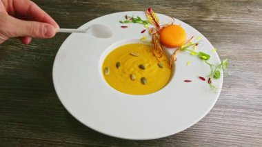İnsan eli beyaz plastik kaşıkla kabak kremalı çorbayı dene.