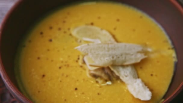 O foco em na sopa de creme amarela saborosa decorada com cogumelos e pão secado — Vídeo de Stock
