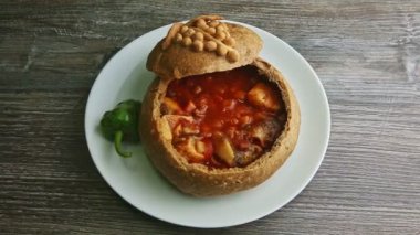 top view on trendy decorated fish soup in original brown bread bowl on white plate