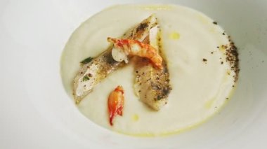 closeup rotates white plate with fish cream soup decorated with prawns and spices