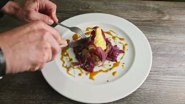 Mensenhanden snijd klein stukje gebakken vlees met vork en mes op bord — Stockvideo
