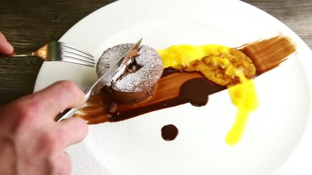 Primo piano mani umane tagliare torta al cioccolato a metà con forchetta e coltello — Video Stock