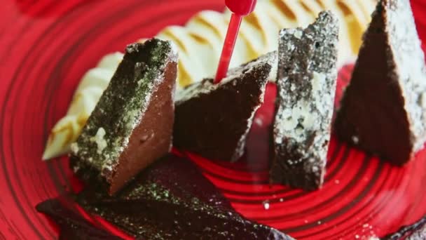 Torta brownie affettata primo piano finemente decorata con crema che gira sul piatto rosso — Video Stock