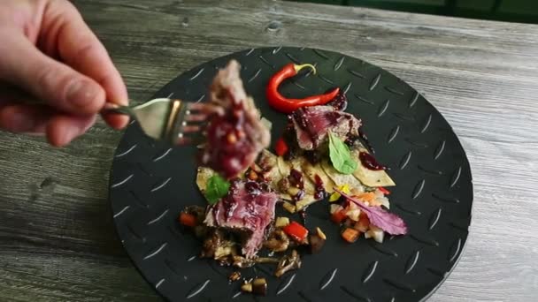 Mano humana quita pequeña rebanada de carne horneada pieza por tenedor de plato negro — Vídeo de stock