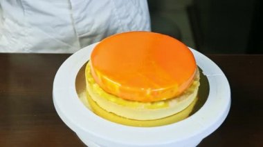 confectioner decorating round cheesecake with orange mirror glaze on white stand
