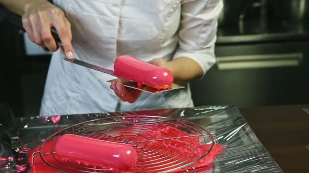 Confectioner in white uniform put pink glazed oval mousse cake on golden stand — Αρχείο Βίντεο