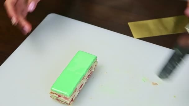 Confectioner takes portion of green glazed layered cake and put on small golden stand — Stockvideo