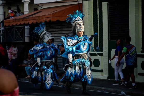 在多米尼加狂欢节上，一群身着各式服装的人走过城市街道 — 图库照片