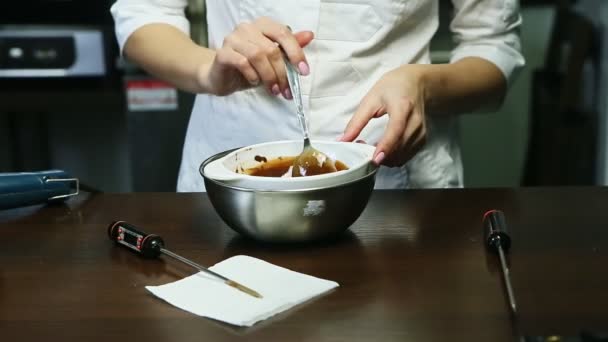 Кондитер перемешивается большой ложкой жидкой шоколадной глазури в глубокой белой миске — стоковое видео