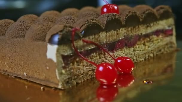 Closeup hand rotates plate with half of chocolate cream cake with cherry interlayer — Stock video