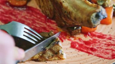 closeup human hands cut off small piece from barbecued meat rib by knife on plate