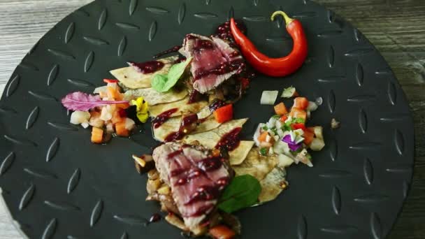 Hand rotates black plate with grilled meat pieces, potato chips, and vegetable salad — ストック動画