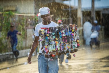 Concepcion De La Vega, DOMINICAN REPUBLIC - FEBRUARY 11, 2019: black man sells assorted sunglasses under strong rain on dominican city street on February 11 in Concepcion De La Vega