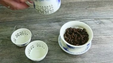 human hand puts two small cups and pours hot tea from teapot there