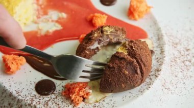 closeup hand shows sliced half of chocolate dessert by fork and knife