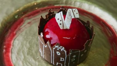 slow zoom out from red glazed dessert with chocolate castle rotates on golden plate