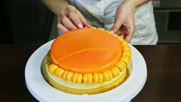 Confectioner decorate orange glazed round cheesecake by small yellow macaroons — Stockvideo