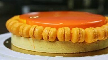 closeup round orange glazed cheesecake with mini macaroons rotates around