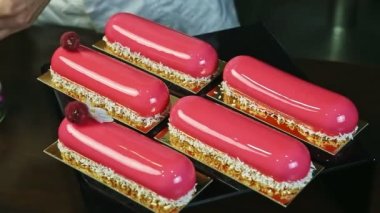 confectioner decorates by violet flower one of five pink glazed eclairs with raspberries
