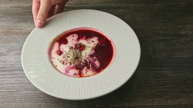human hand rotates plate with traditional ukrainian borscht decorated with sour cream