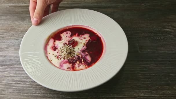 Human hand rotates plate with traditional ukrainian borscht decorated with sour cream — 图库视频影像