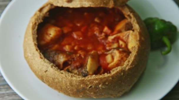 Top view focus in at exquisite decorated fish soup in brown bread bowl on white plate — Stock video