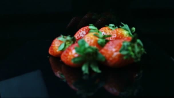 Focus in at pile of fresh juicy whole red strawberries lie on black background — Stockvideo