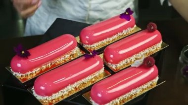 confectioner shows five pink glazed oval cakes decorated with raspberries and flowers