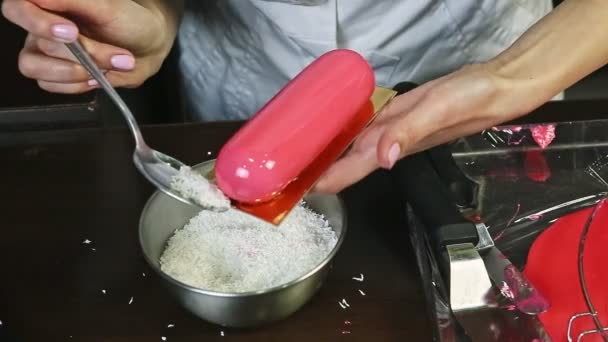 Крупным планом женские руки украшают розовый овальный торт кокосовой стружкой — стоковое видео
