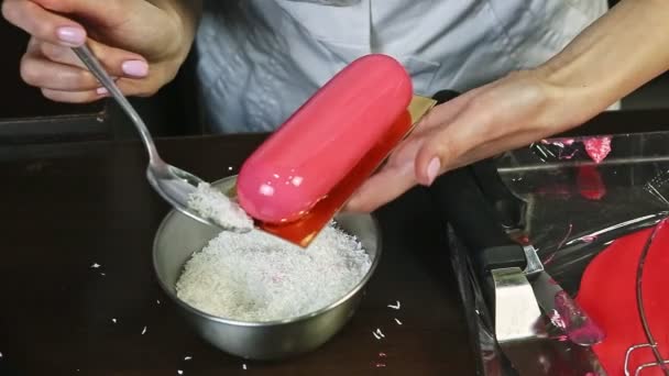 Closeup female hands decorate pink glazed oval cake with coconut shavings — Αρχείο Βίντεο