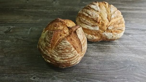 Два хлеба цельного круглого пшеничного хлеба на деревянном столе — стоковое видео