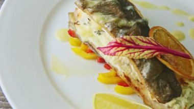 top view closeup trendy decorated grilled sea fish on sliced peppers rotates on plate
