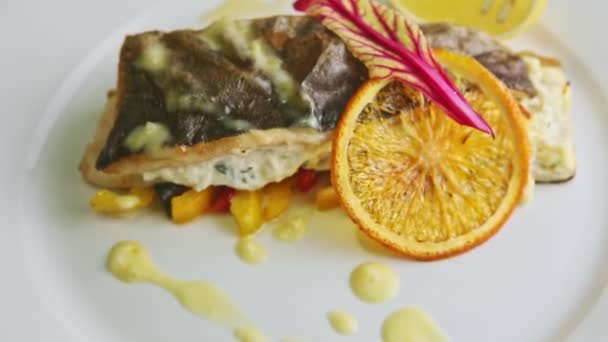 Closeup exquisite decorated roasted sea fish on sliced peppers rotates on plate — Stock Video