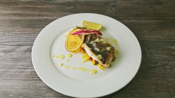 Zoom in at finely decorated stuffed grilled sea fish on sliced peppers rotates on plate — Stok video