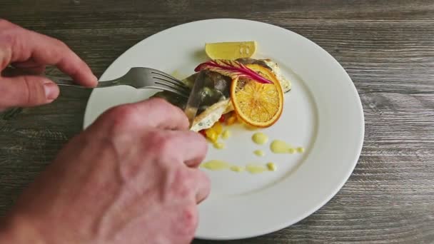 Hands slice on halves by fork and knife baked sea fish served on white plate — Stok video