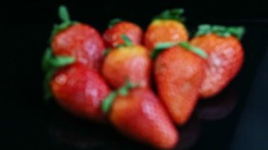 top view focus in at group of whole ripe red strawberries on black mirror surface