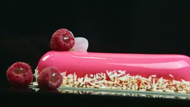 Closeup panorama at pink glazed long oval cake with coconut shavings and raspberry — Stockvideo