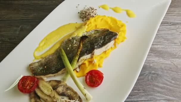 Tasty grilled white fish fillet on potato purre and sliced vegetables rotates on plate — 图库视频影像