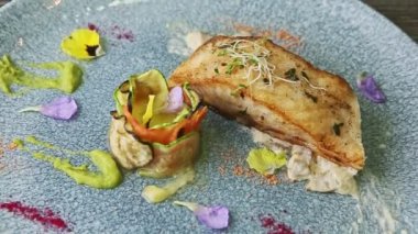 top view closeup roasted sea fish steak with sauce and grilled vegetables on blue plate