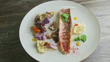 top view on finely decorated grilled fish fillet with sliced vegetables rotates on plate