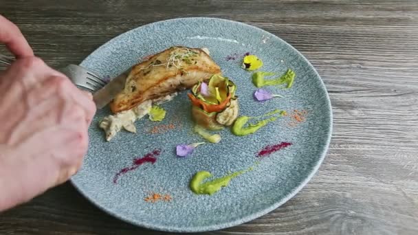 Hands cut off small piece from roasted fish steak by knife and fork on blue plate — Stok video