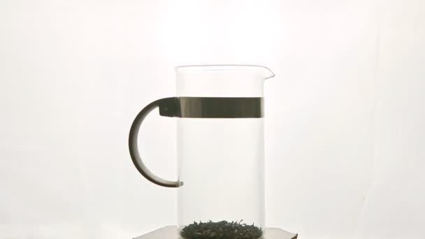 grande théière en verre avec feuilles de thé tournant autour sur piédestal contre blanc 