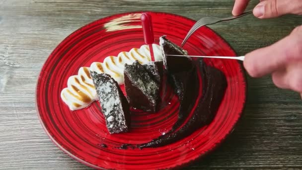 Mano umana fetta da forchetta e coltello torta brownie con crema bianca su piatto rosso — Video Stock