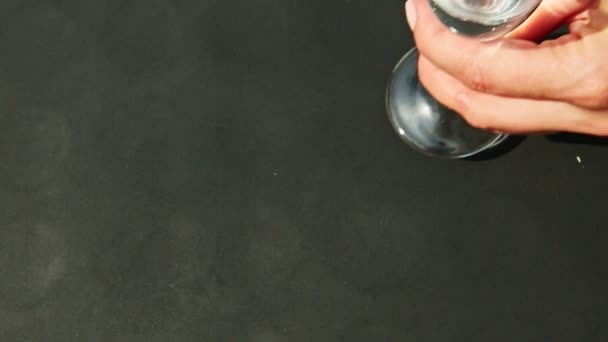 Draufsicht auf weibliche Hand stellt ein hohes Kristallweinglas mit Wasser auf schwarzen Tisch — Stockvideo