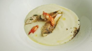 Yakından çekilen el, karides ve baharatla süslenmiş bir kaşık balık kremalı çorba ile dener.