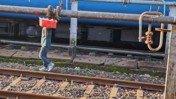 Guy draagt rode doos langs spoorbanen Voorbij metalen buizen — Stockvideo