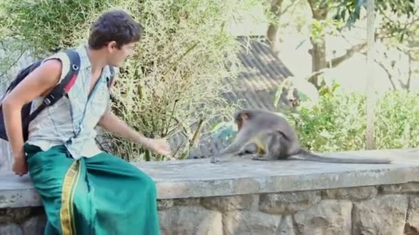 Guy Tourist Sits karmi małpę kamienną zaporą w parku — Wideo stockowe
